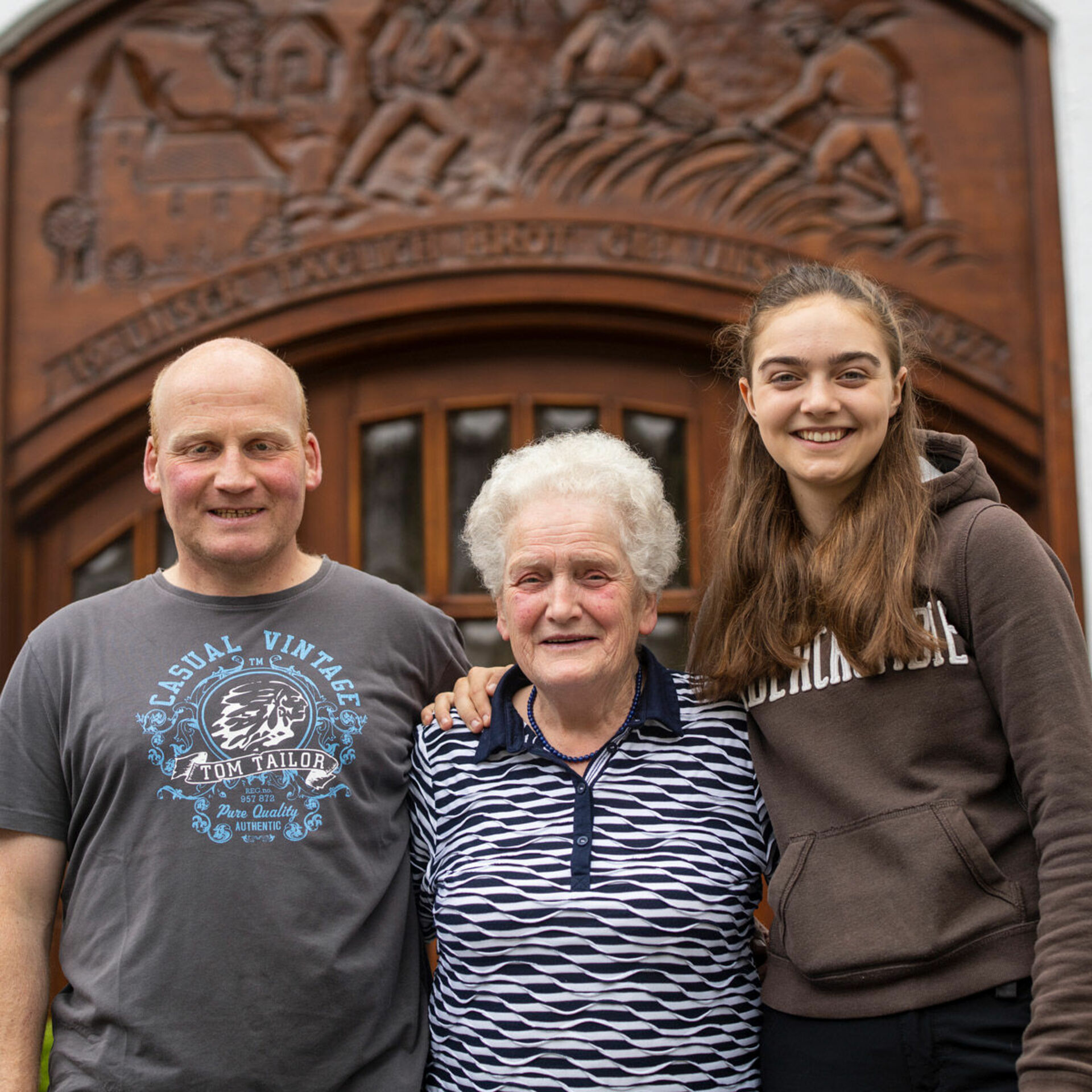 Gastgeberfamilie mit 3 Personen vor Holztür 