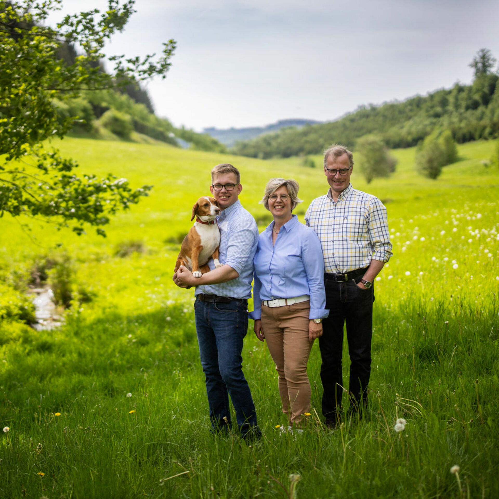 Gastgeberfamilie bestehend aus 3 Person stehen dauf Wiesen, Links Mann mit Hund 